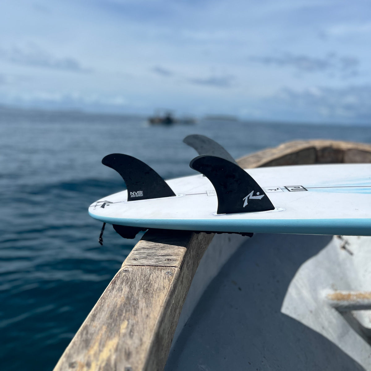 Picture of Rusty Thruster Fin Set up close attached to a board laying on the top of a boat in the water.